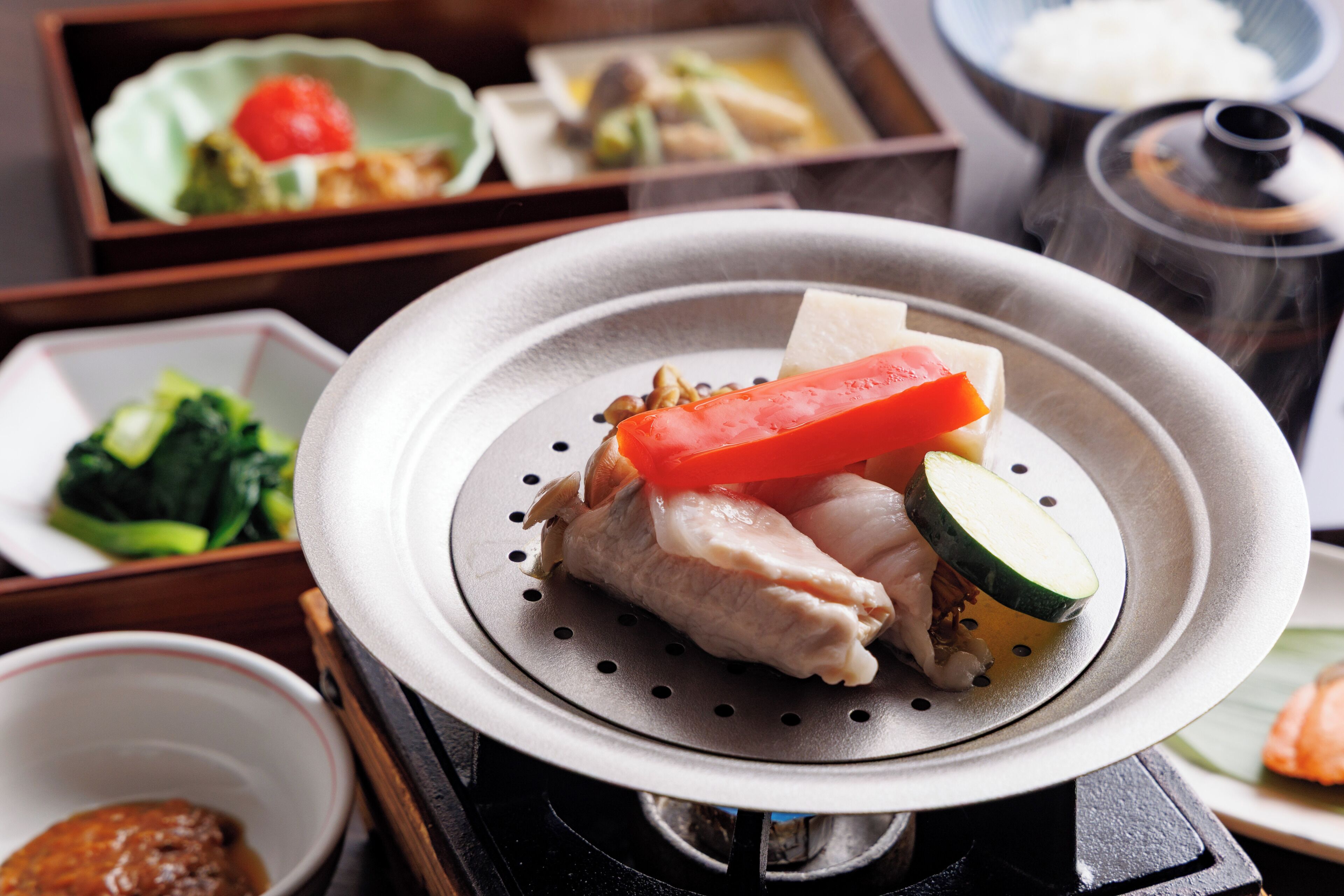 A dining setup with a hot plate, various dishes including fish, vegetables, and a bowl of sauce.