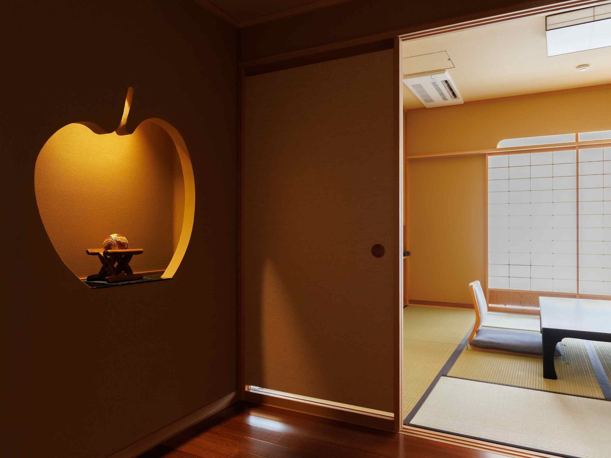 A room with a tatami mat floor, a low table, and a sliding door with a view of a traditional Japanese room.