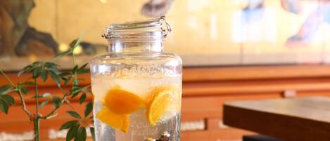 A clear glass jar with a metal clasp, filled with water and orange slices, placed on a table with a plant beside it.