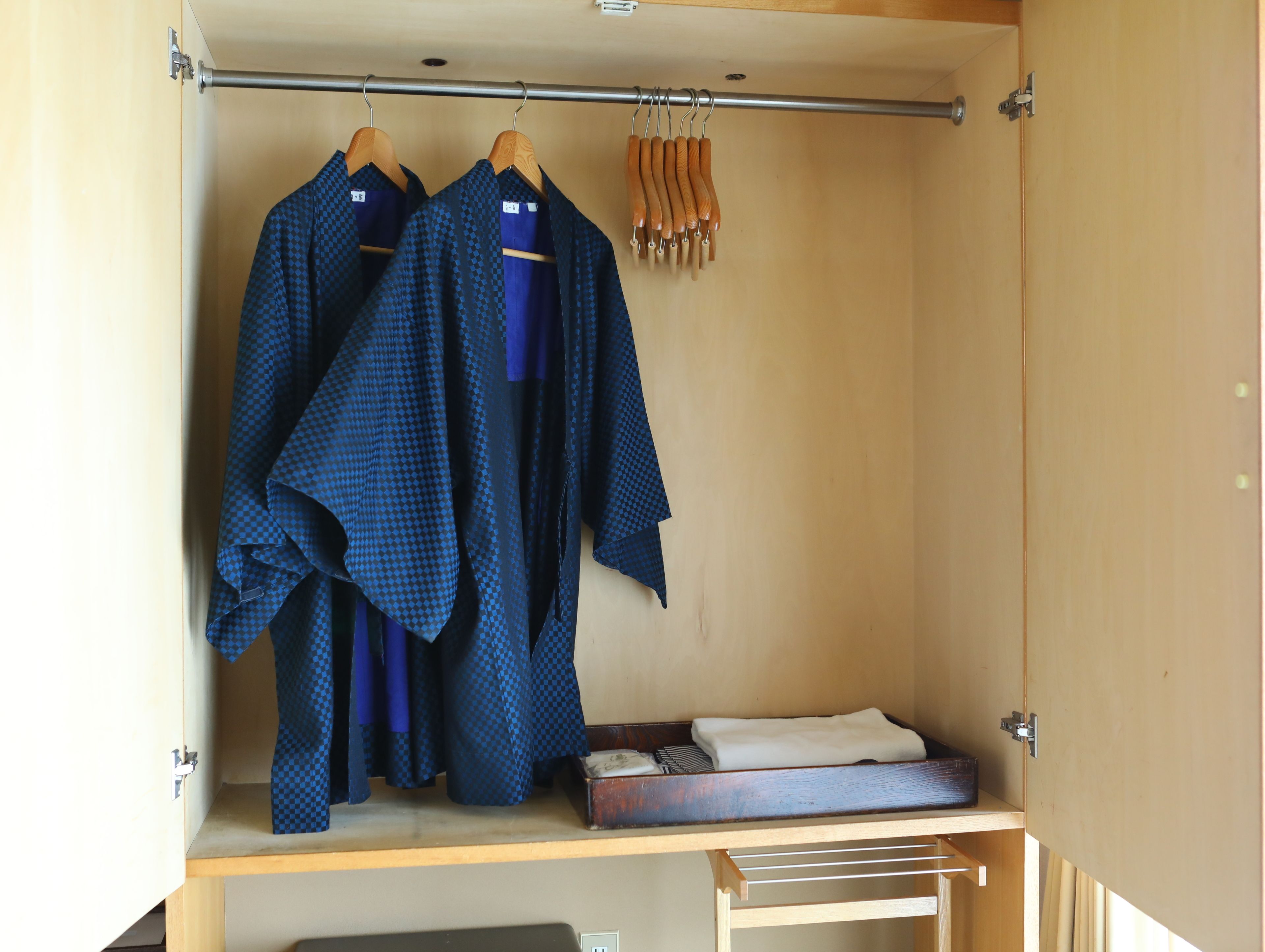 A wardrobe with two hanging robes and a wooden shelf with a folded robe and a small box.