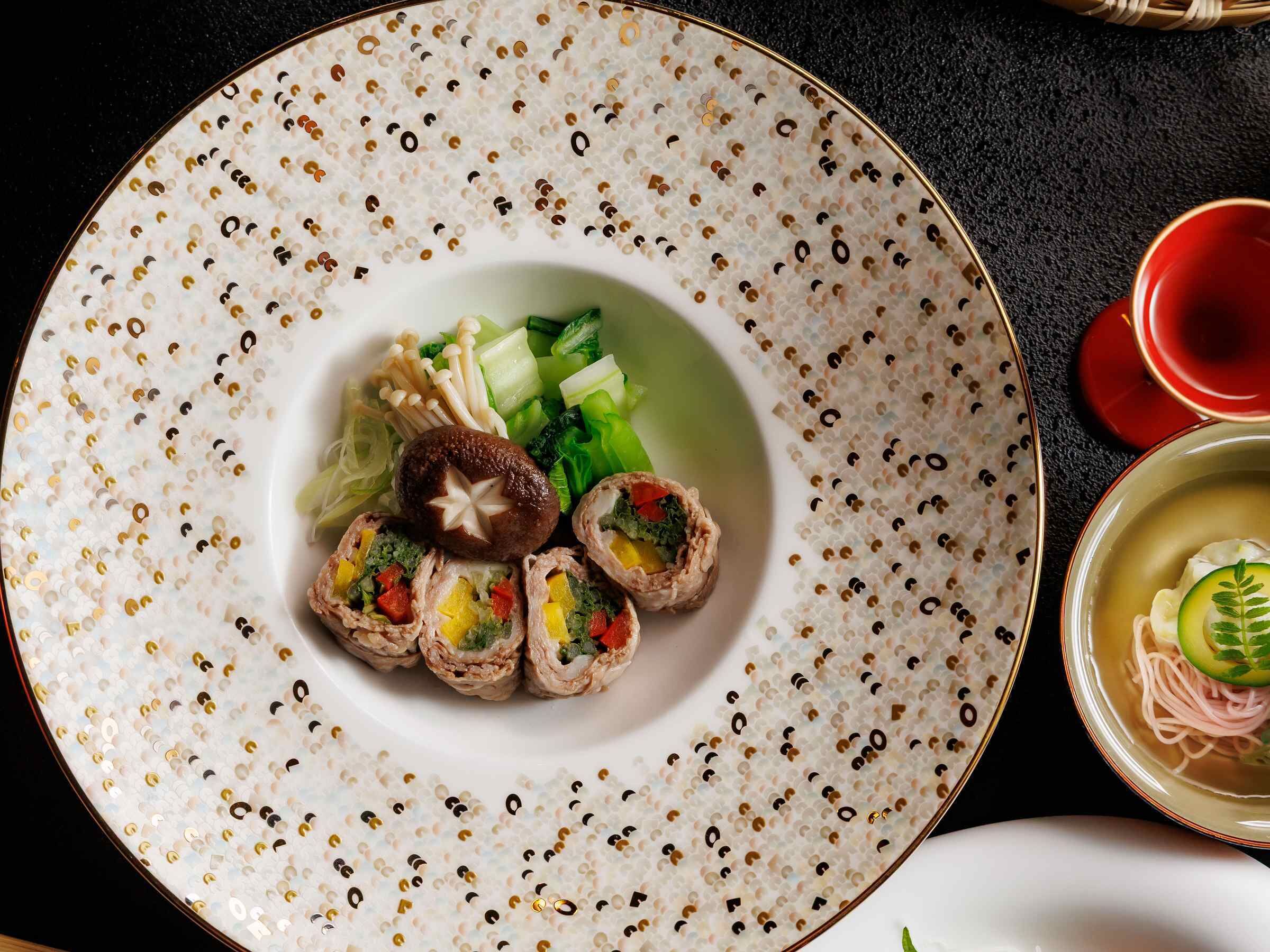 A plate with food, a bowl of soup, and chopsticks on a table.