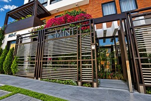 A modern hotel entrance with a metal gate, greenery, and a clear sky.