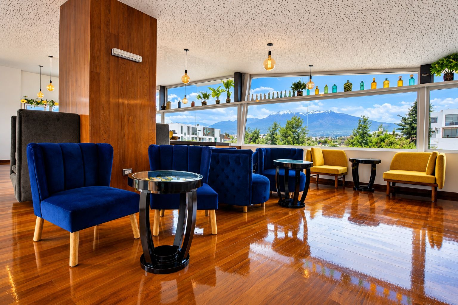 Un área de estar moderna con sillones tapizados en azul y amarillo, suelo de madera y un amplio ventanal con vistas a la montaña.