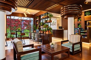 Un moderno vestíbulo de hotel con mobiliario de madera, un mostrador de recepción y un gran ventanal con vistas a flores rojas.