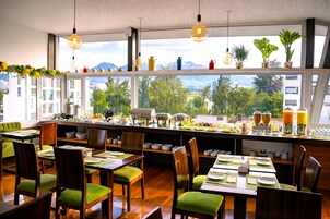 Un comedor con mesas dispuestas para el desayuno, vistas de montañas a través de amplias ventanas y varios electrodomésticos en la encimera.