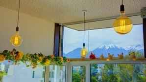 A room with a view of snow-capped mountains through a large window, a ceiling with a dotted pattern, and hanging light fixtures.