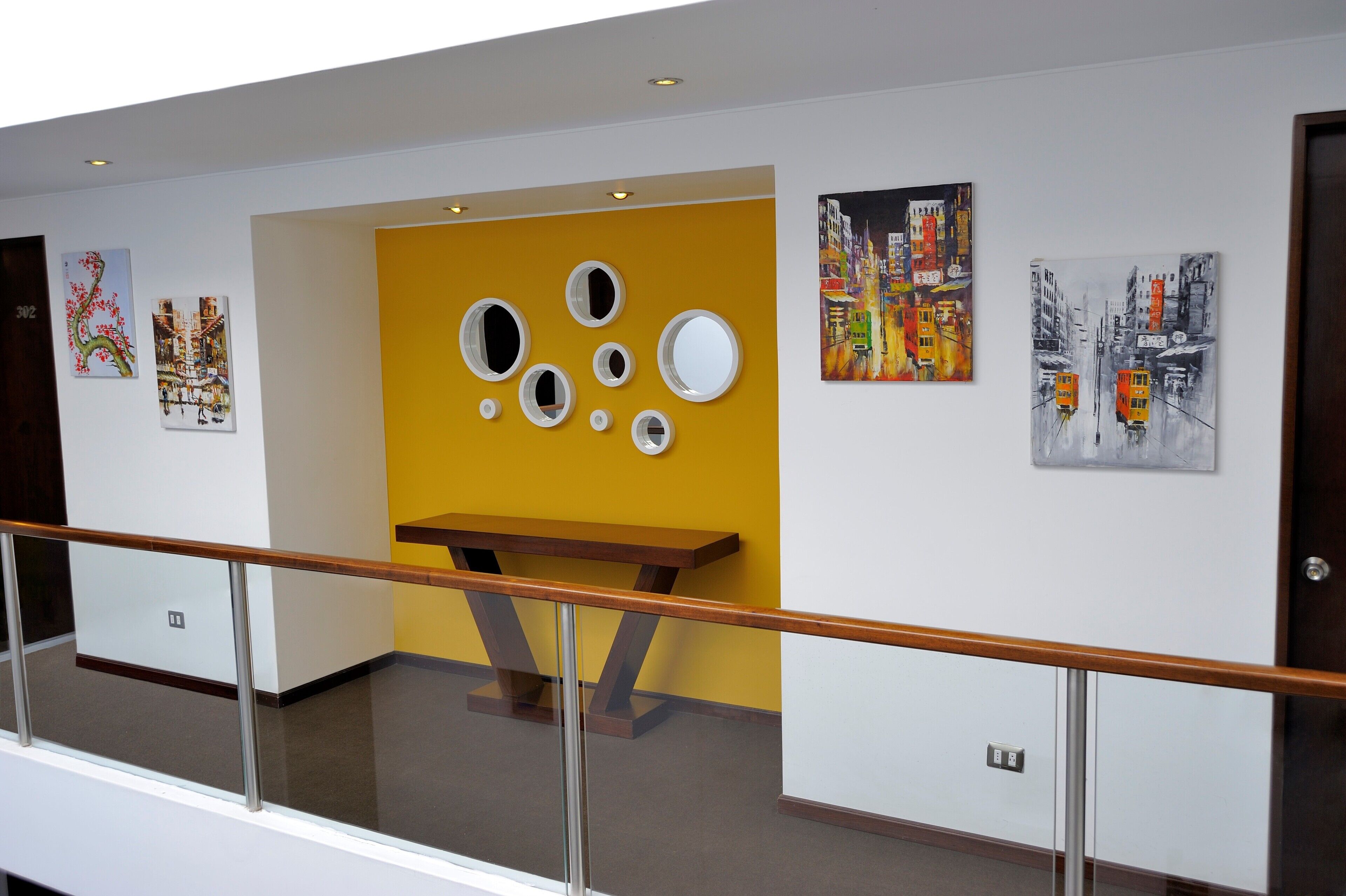A corridor with artwork on the walls, a wooden bench, and a railing.