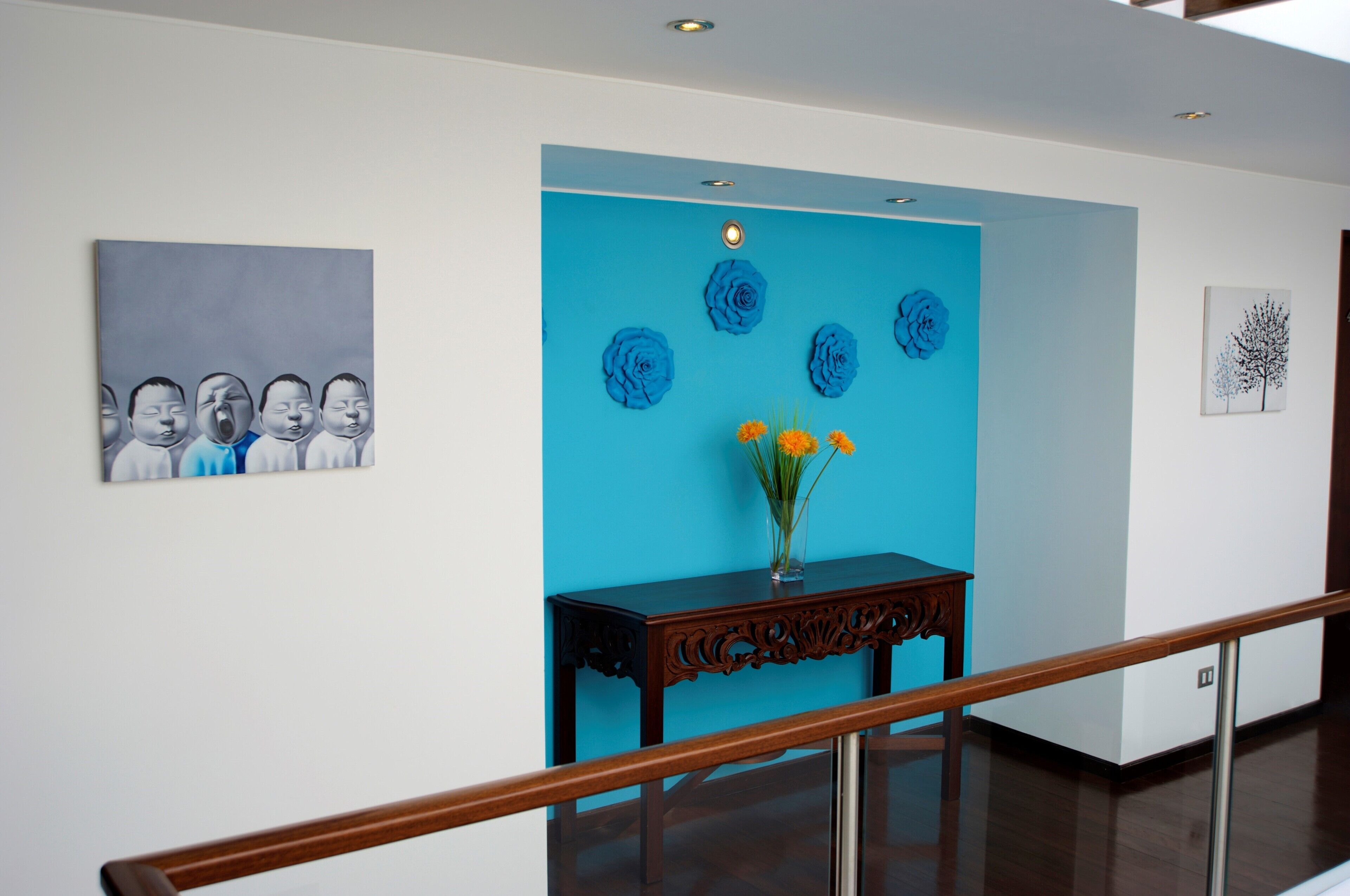 A hallway with a blue accent wall, a wooden console table with a vase of flowers, and artwork on the walls.