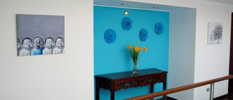 A hallway with a blue accent wall, a wooden console table with a vase of flowers, and artwork on the walls.