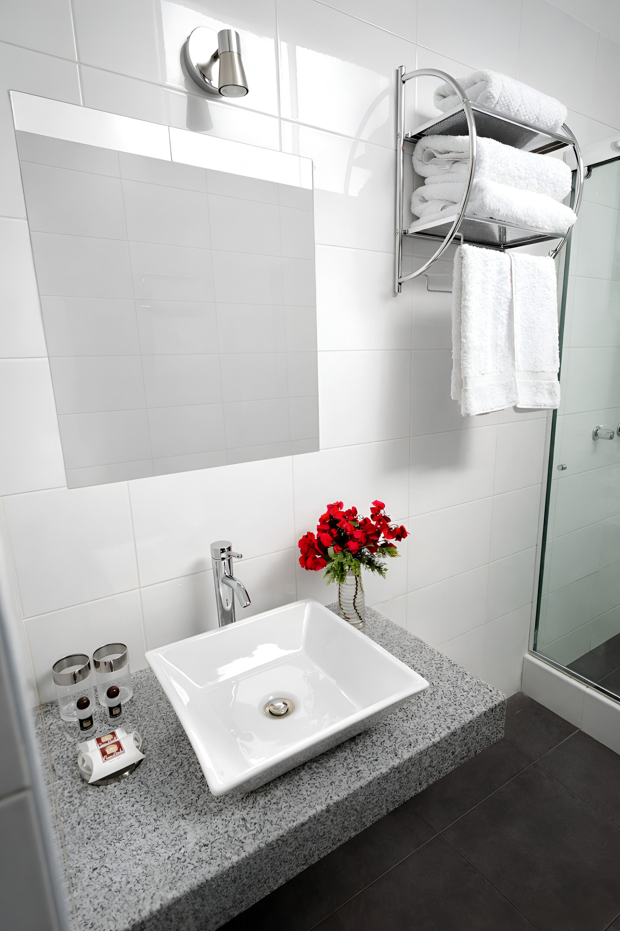 A modern bathroom with a white sink, a glass shower enclosure, and a towel rack with folded towels.