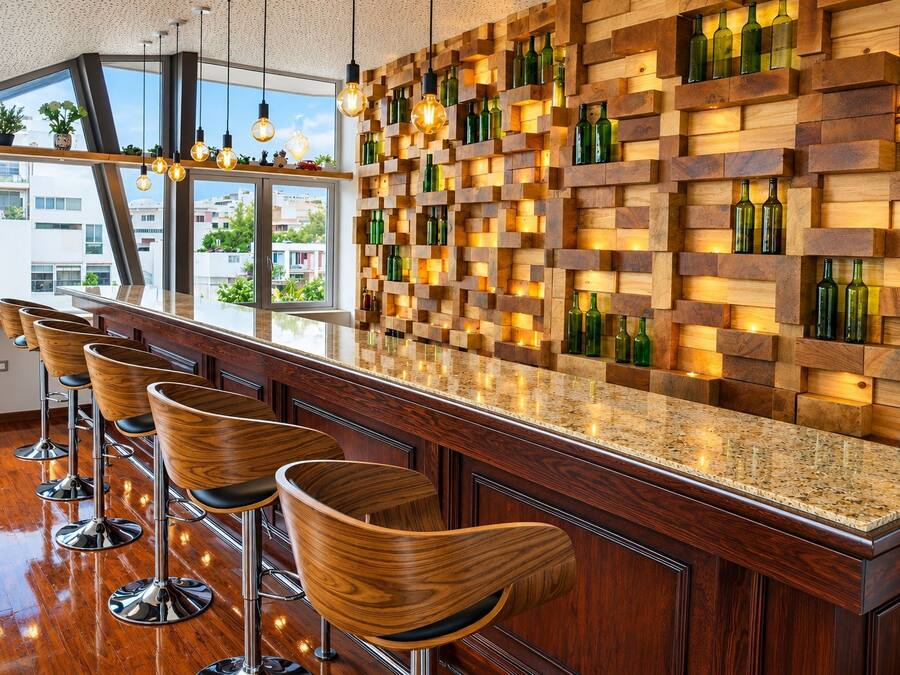 Una zona de bar con estantes de madera que sostienen botellas, encimera de granito pulido y taburetes de bar modernos.