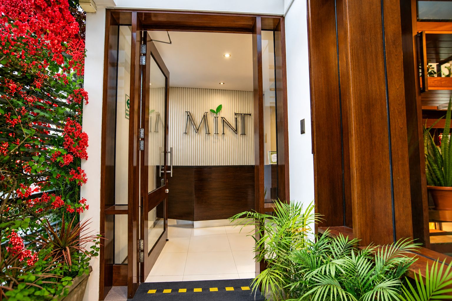 Entrada de hotel con puerta de madera, una recepción y un cartel que dice 'MINT'.