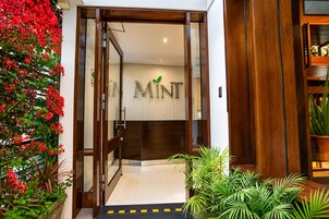 Entrada de hotel con puerta de madera, una recepción y un cartel que dice 'MINT'.