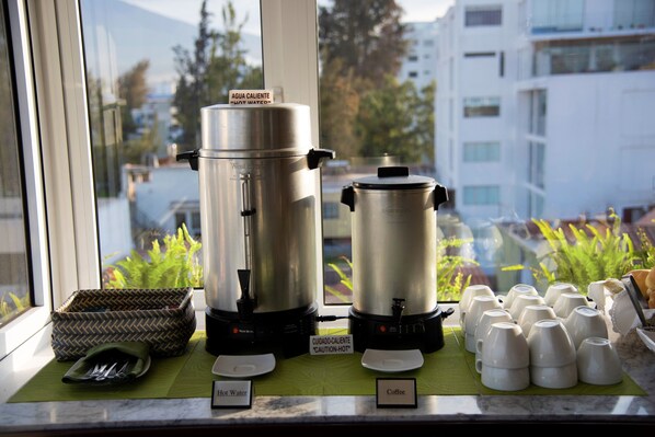 Dos cafeteras sobre una encimera, con vistas a edificios y plantas al exterior.