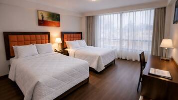 A hotel room with two beds, a desk, and a large window with curtains.