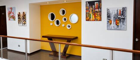 A hallway with artwork on the walls, a wooden bench, and a railing.