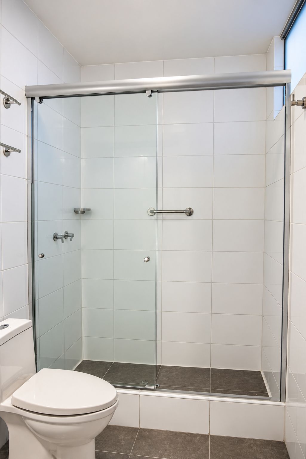 Un baño con ducha de mampara de vidrio, azulejos blancos y un inodoro blanco.
