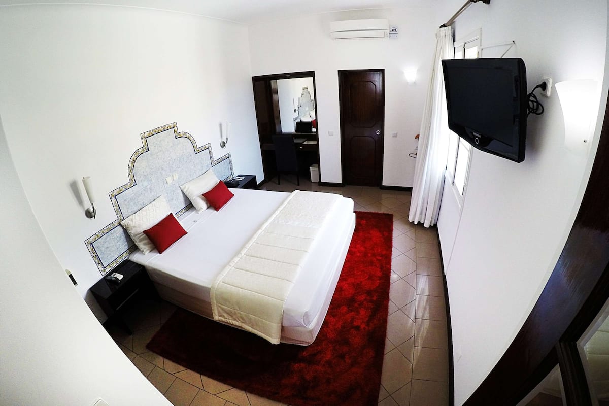 Una habitación de hotel con una cama, televisor, escritorio y puerta.