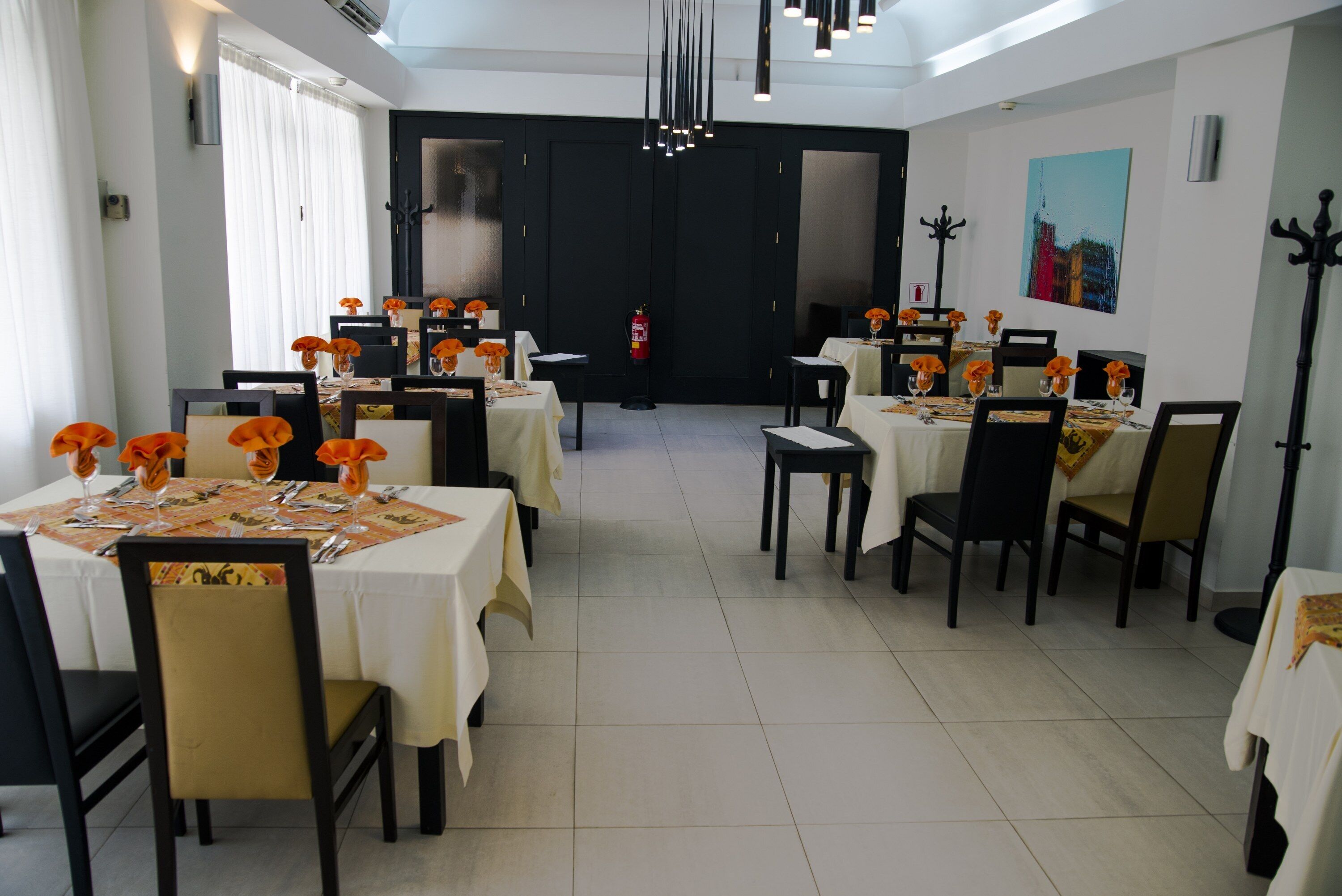 A dining area with multiple tables set for service, chairs, and a fire extinguisher.