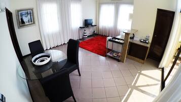 A compact hotel room with a dining area, a TV, a small kitchenette, and a red rug.