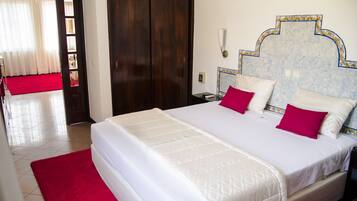 Habitación de hotel con una cama grande, alfombra roja, armario de madera y pared de azulejos con un borde decorativo.