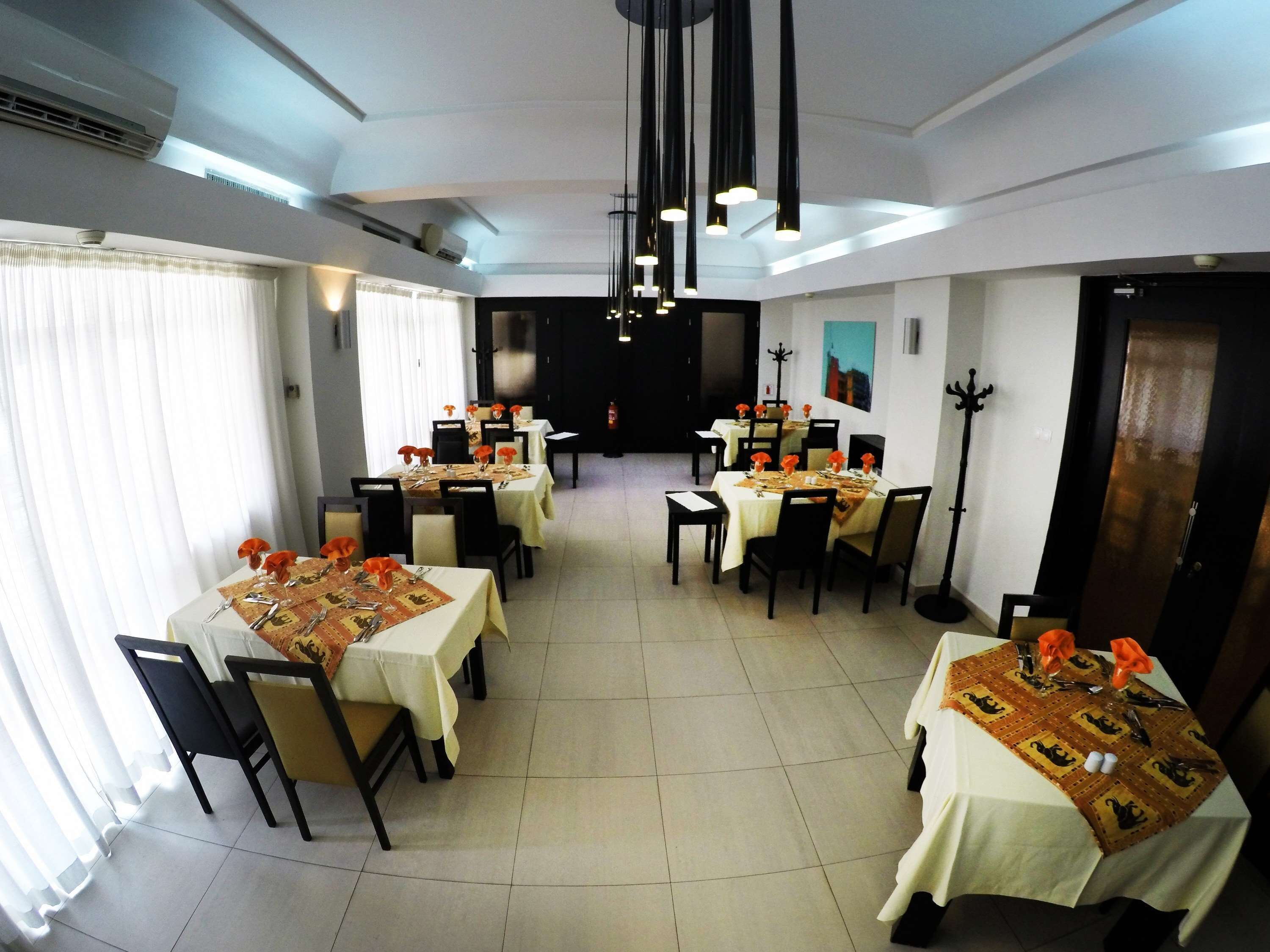 Un espace repas avec plusieurs tables dressées pour les convives, présentant un design moderne avec des nappes blanches et des serviettes orange.