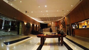 A spacious lobby with a central wooden table, a reception desk, and a staircase leading to upper floors. - Hotel Continental (Luanda)