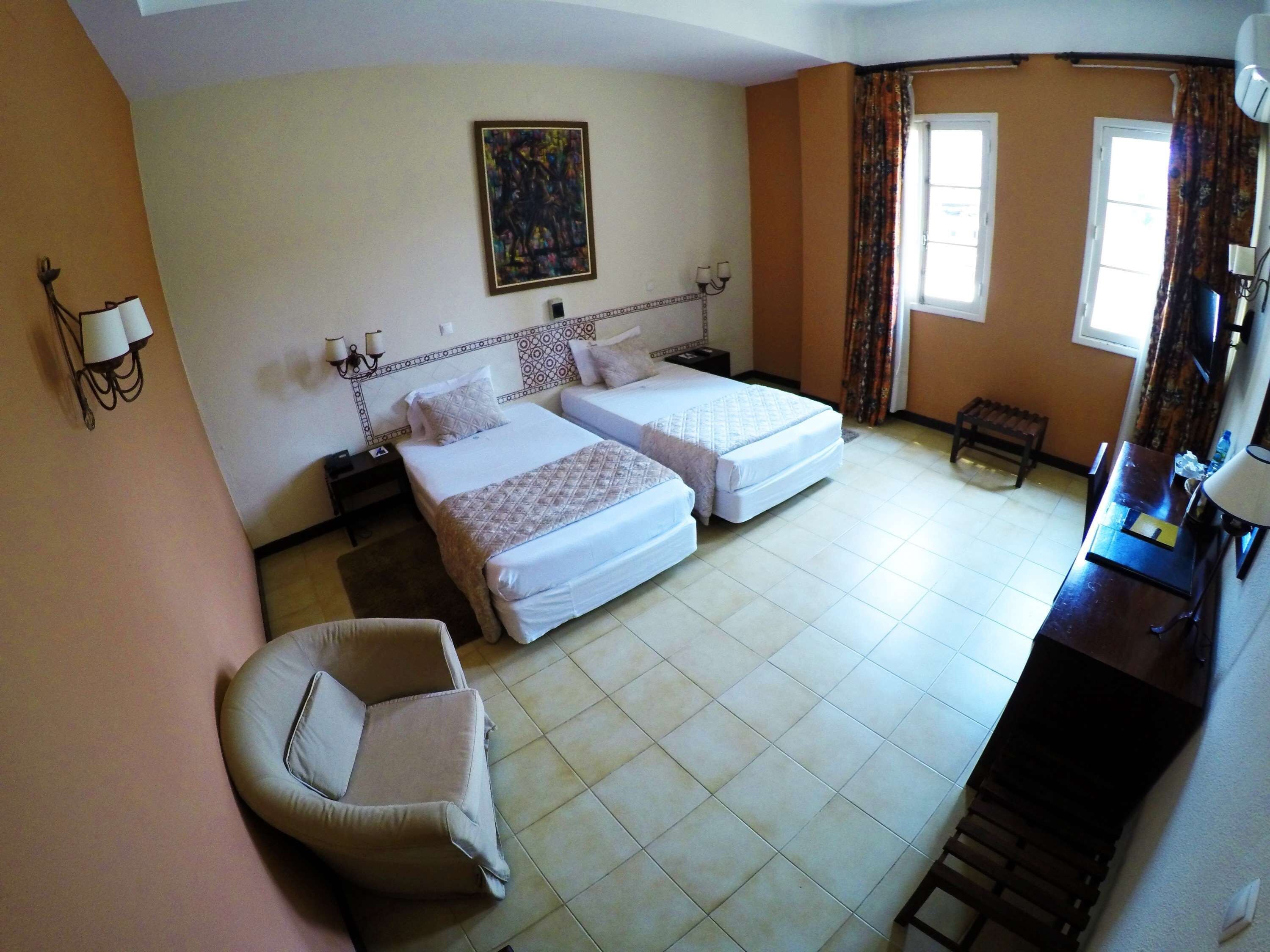 A hotel room with two beds, a chair, a desk, and a painting on the wall.