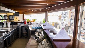 A commercial kitchen with stainless steel appliances, a bar area with a menu, and a view of the city through large windows. - Hotel Continental (Luanda)