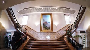 A grand staircase with a central view of a framed landscape painting, surrounded by patterned walls and a polished floor. - Hotel Continental (Luanda)