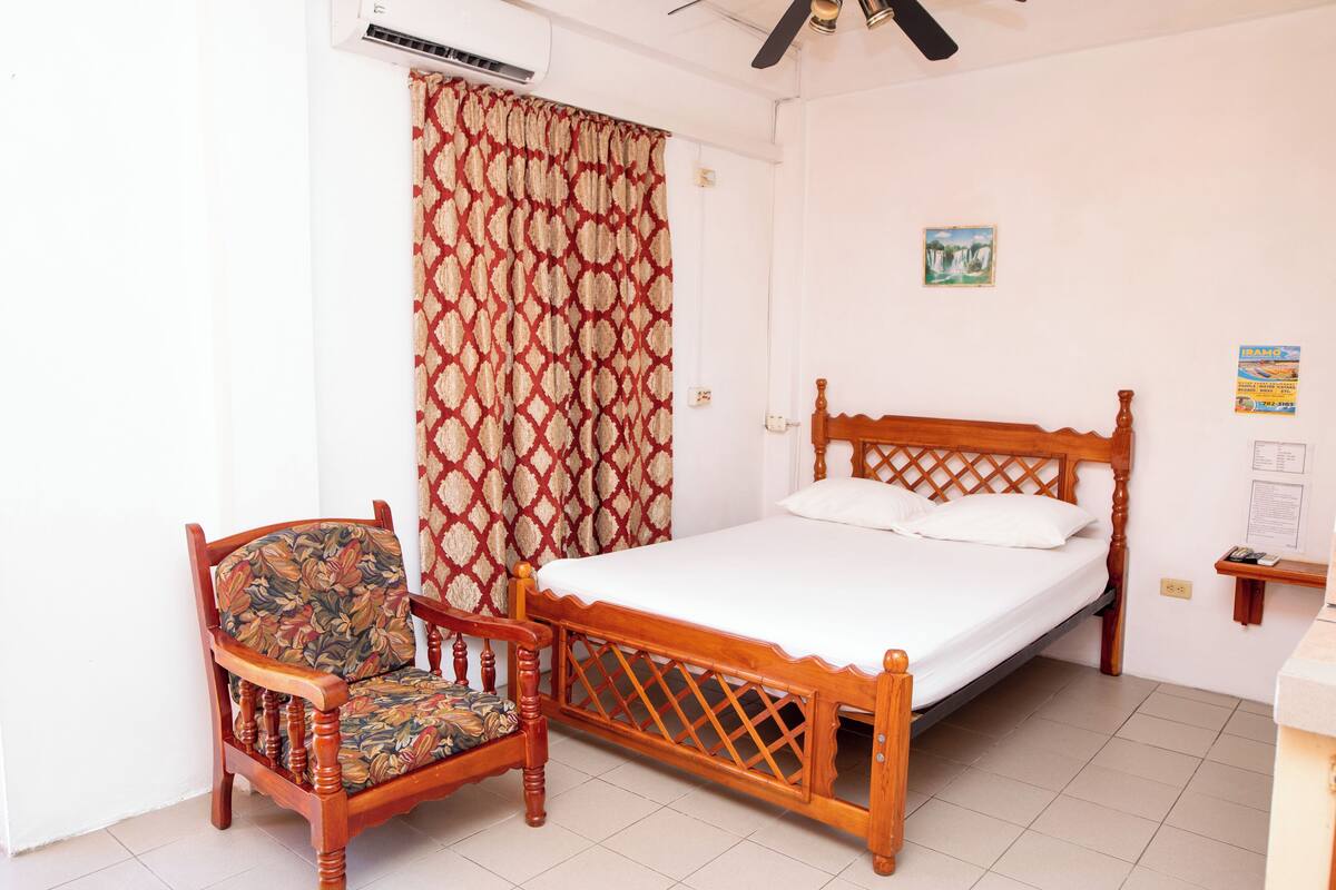 A bedroom with a wooden bed, a floral upholstered chair, and a patterned curtain.