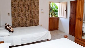 A bedroom with two beds, a wooden wardrobe, a door leading to a balcony, and a floral curtain.
