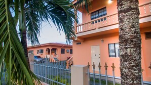 A two-story building with a balcony, a car parked in front, and a palm tree in the foreground.