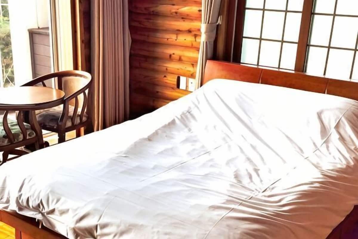 A wooden cabin room with a bed, a small table, and a chair.