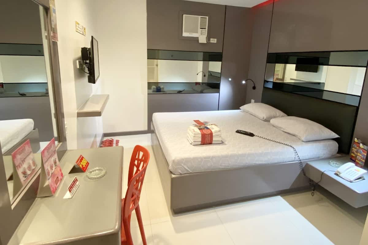 A modern hotel room with a bed, a desk, a chair, and a small table.