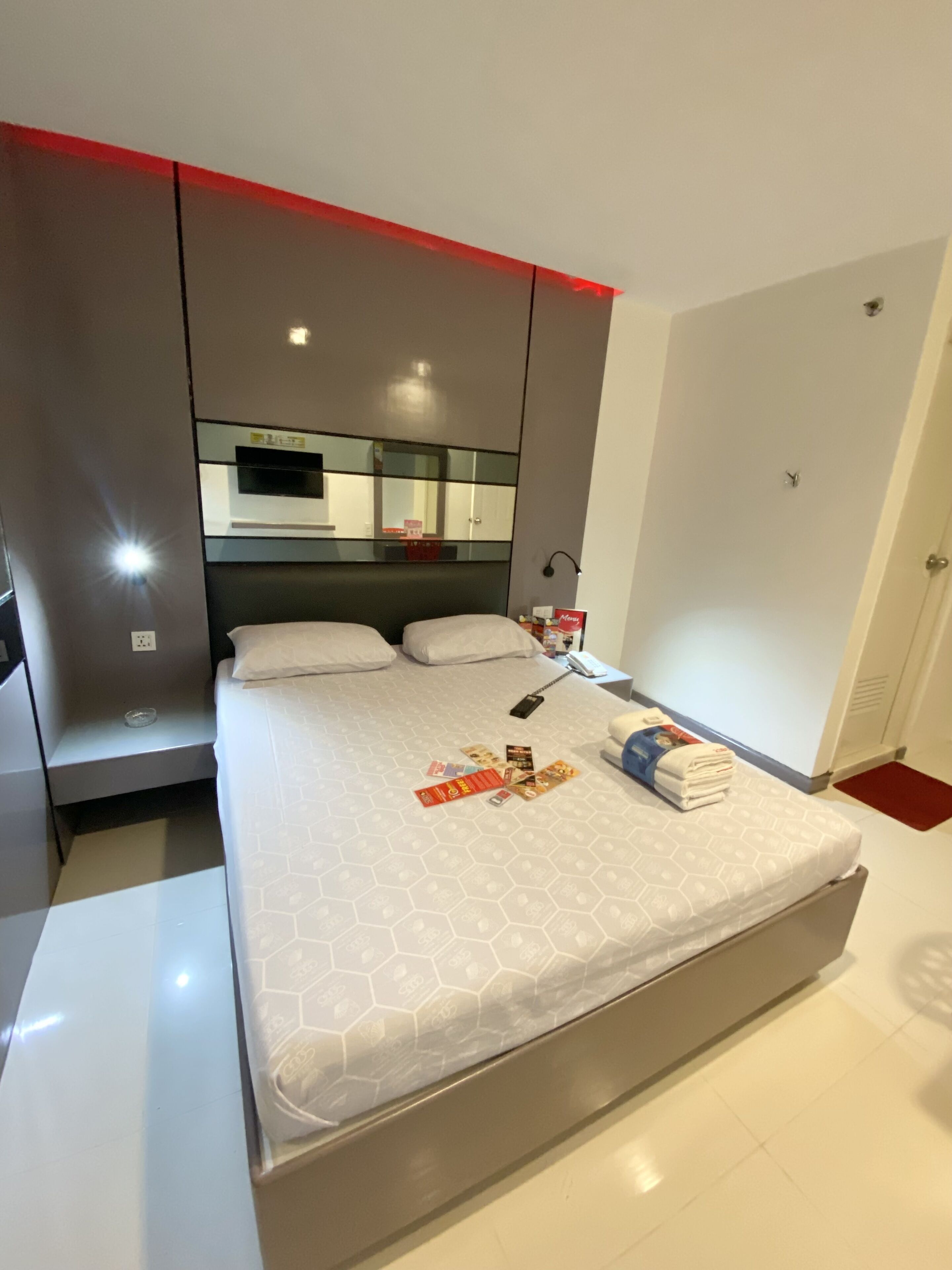 Habitación de hotel moderna con una cama grande, una mesita de noche, un espejo y una pared decorada en rojo.