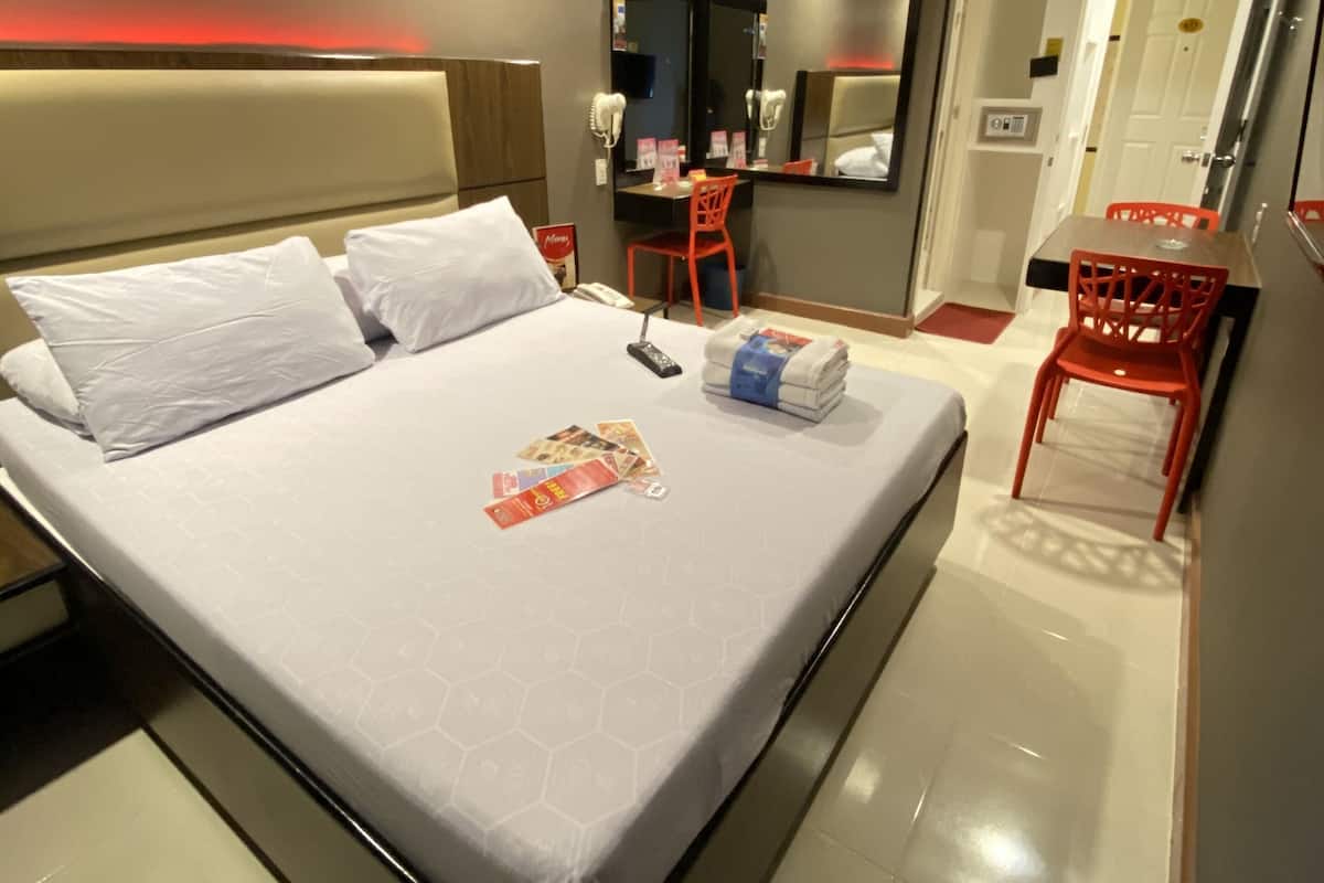 A hotel room with a bed, a desk, a chair, a mirror, and a door.