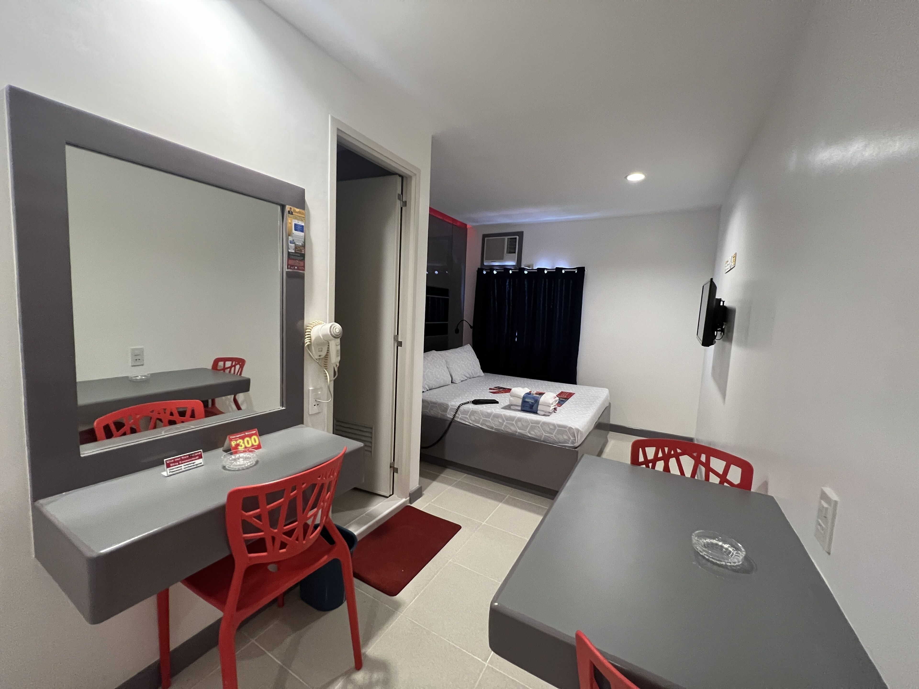Een kleine hotelkamer met een bed, een bureau, een stoel, een spiegel en een kleine kitchenette.