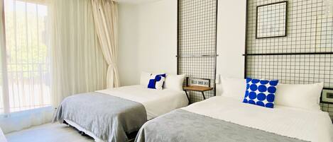 Habitación de hotel con dos camas, una mesita y una ventana con cortinas.