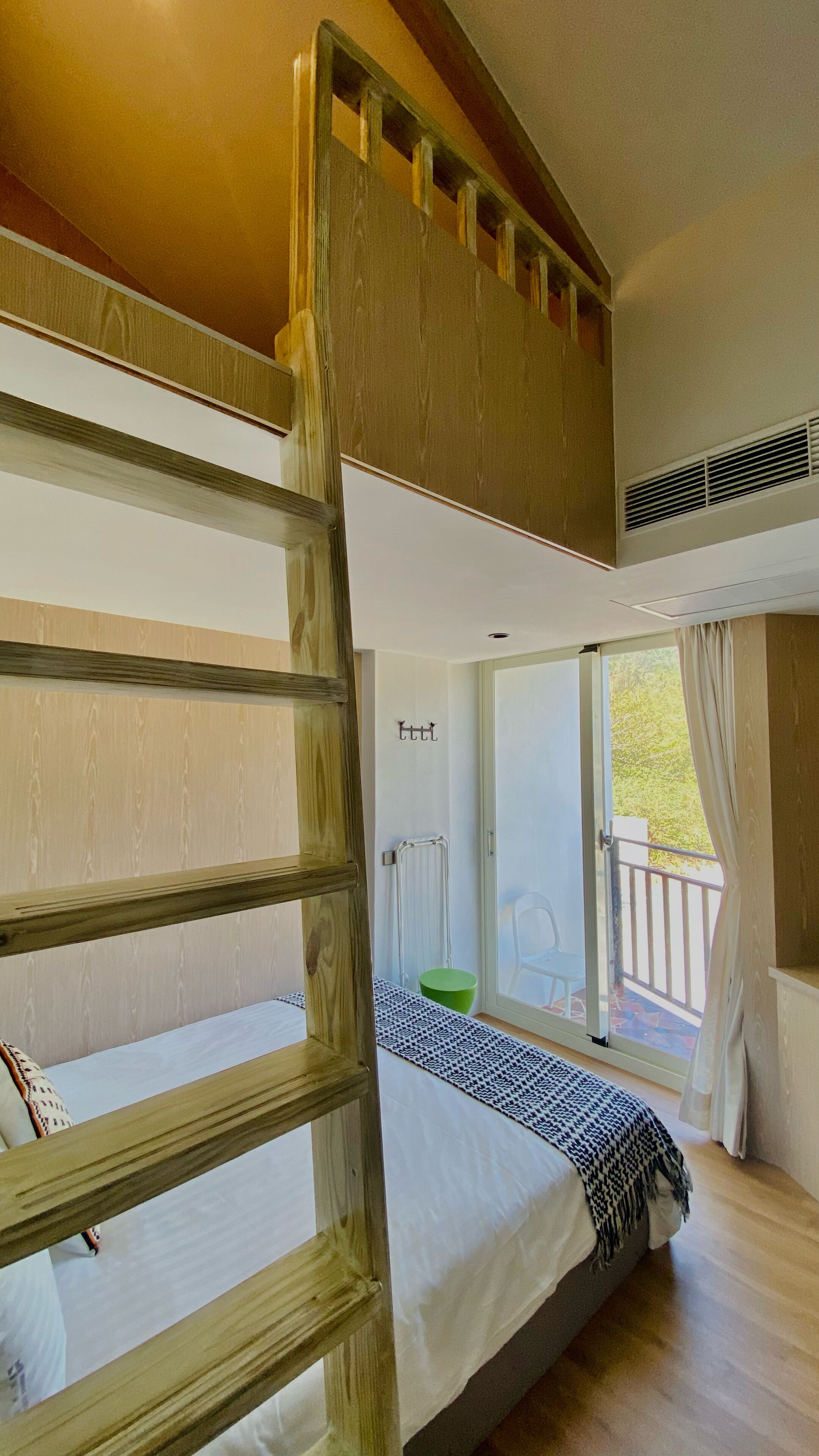 A bunk bed room with a wooden ladder, a radiator, and a window with a view of greenery.