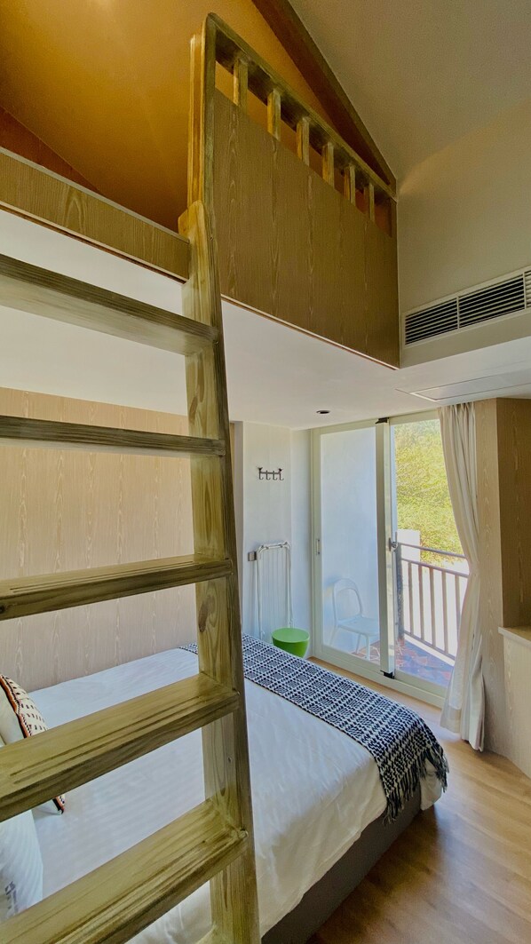 A bunk bed room with a wooden ladder, a radiator, and a window with a view of greenery.
