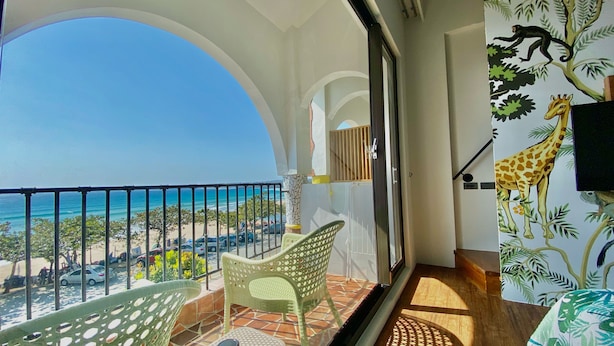 Ein Balkon mit Blick auf den Strand, ein Stuhl und ein Giraffenwandbild.