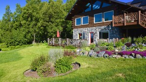 Eine Blockhütte mit Steinunterbau, großen Fenstern und einer Veranda mit Geländer.