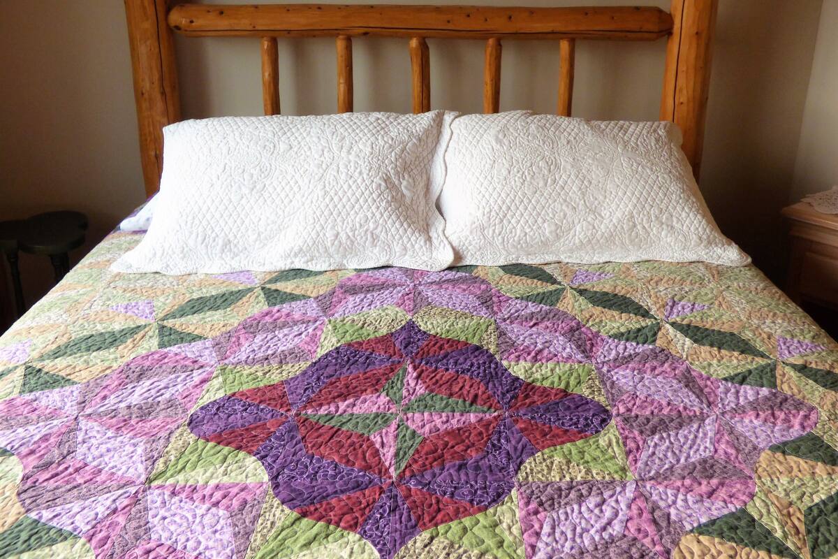 A bed with a wooden headboard, two white pillows, and a colorful quilt.