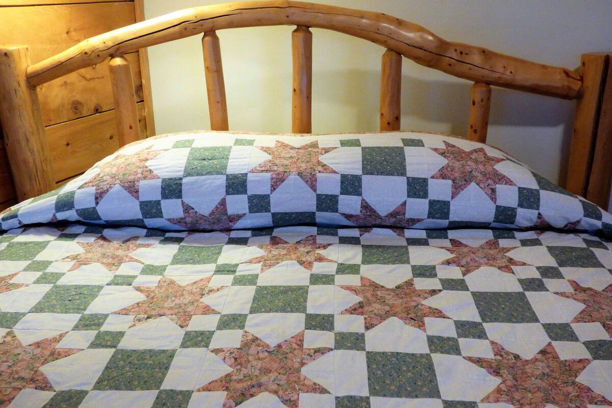 A bed with a quilt featuring a checkered pattern and floral designs.