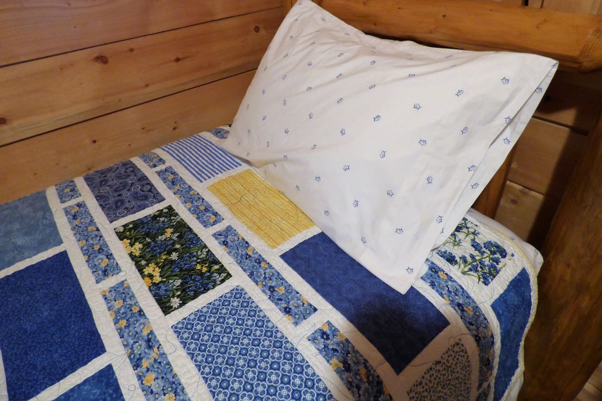 A wooden bed with a quilt featuring various patterns and a white pillow with small designs.