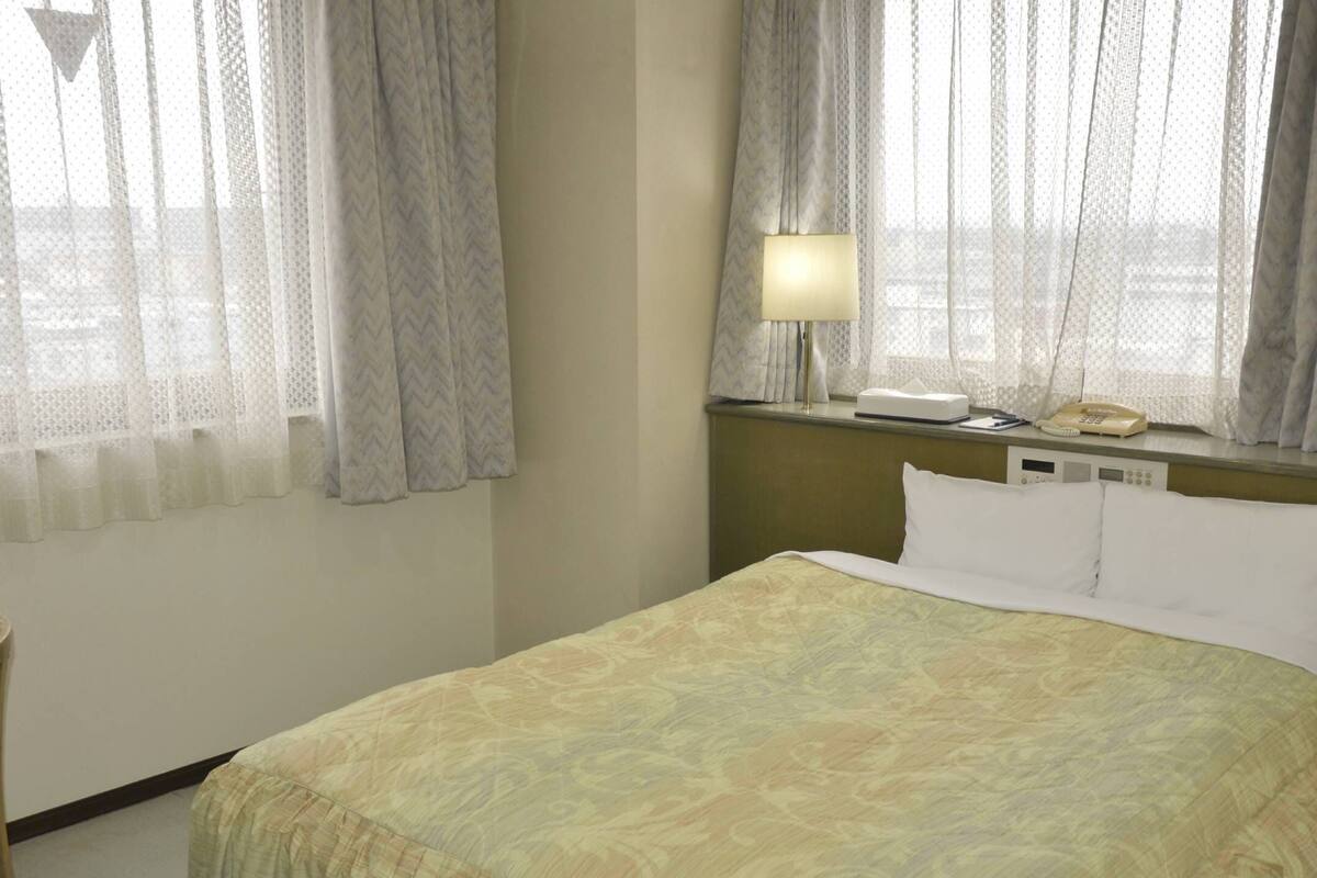 Une chambre d’hôtel avec un lit, une chaise, une table de chevet avec une lampe et un téléphone.