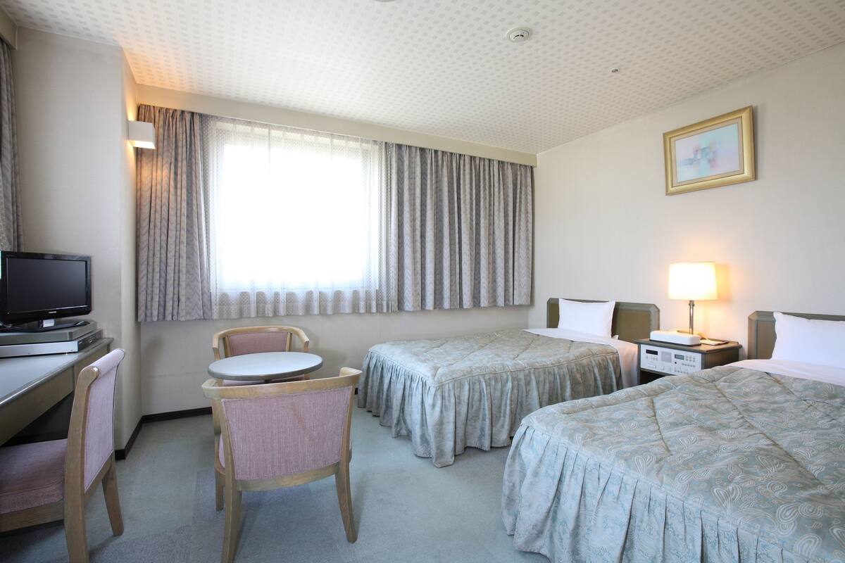 Une chambre d’hôtel avec deux lits, un bureau avec une télévision, une chaise et une lampe.