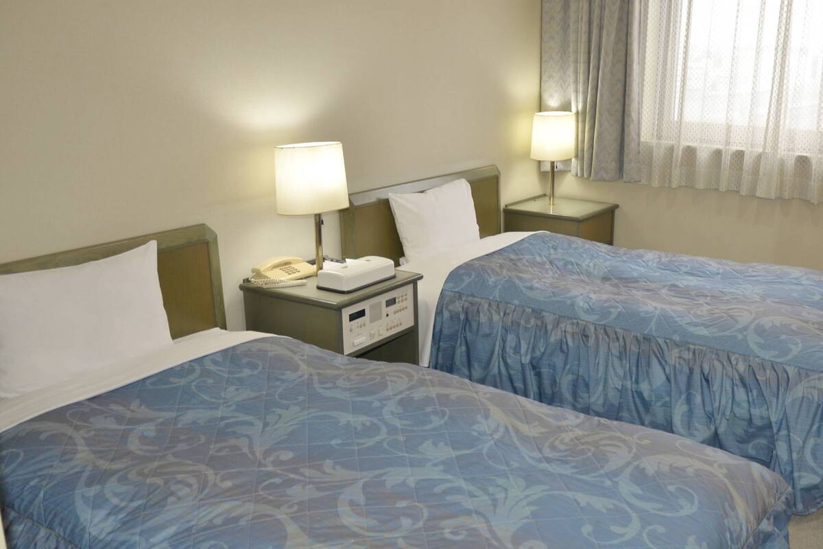 Une chambre d’hôtel avec deux lits, chacun recouvert d’une couvre-lit à motifs bleus, un téléphone sur la table de chevet et une petite table de nuit avec une lampe.
