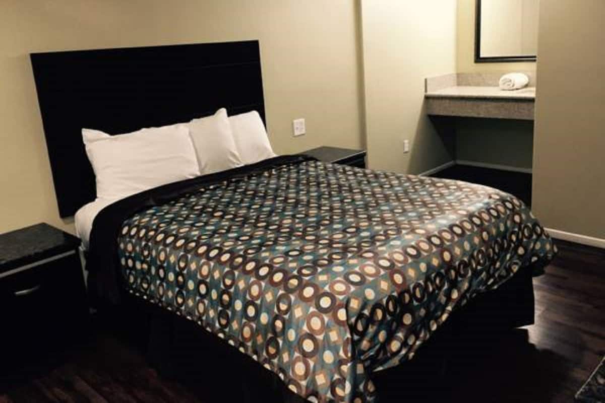 A hotel room with a bed, a nightstand, a dresser, a mirror, and a bathroom with a sink and towel.